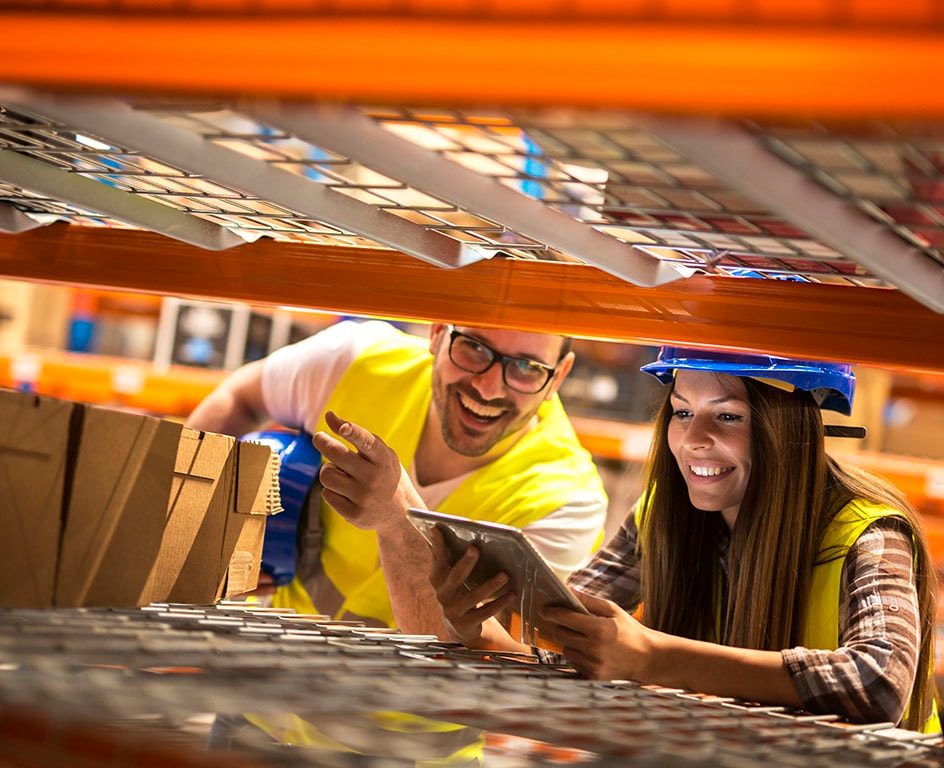 Foto de um homem e uma mulher, trabalhadores de supply, olhando para caixas e um tablet, sorrindo